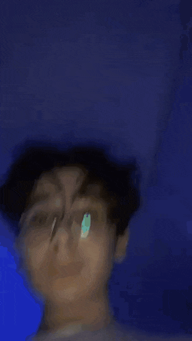 a young man wearing glasses and a white shirt is standing in a dark room .