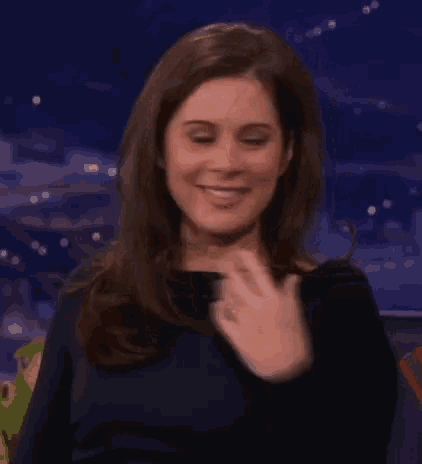 a woman in a black dress is smiling and clapping her hands .