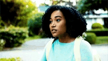 a woman with curly hair wearing a blue shirt and a backpack is walking down a sidewalk .