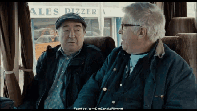 two older men are sitting in front of a sign that says ales pizzar
