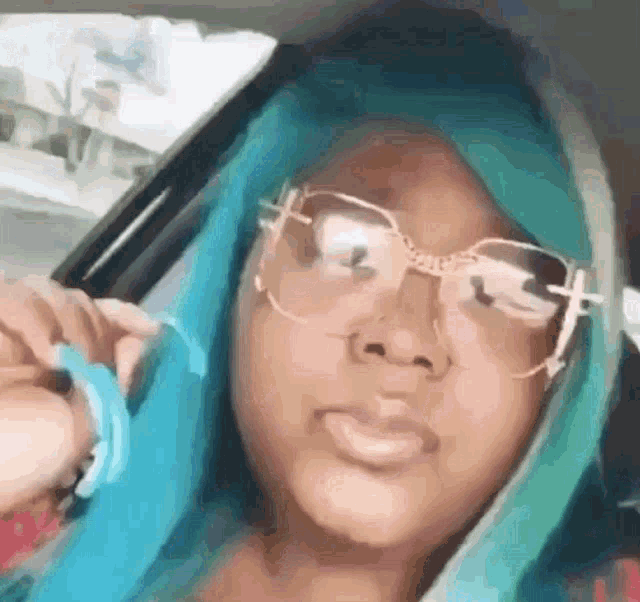 a girl with blue hair and glasses is sitting in a car and taking a selfie .