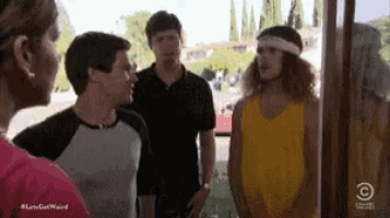 a group of people are standing next to each other and talking . one of the men is wearing a yellow tank top .