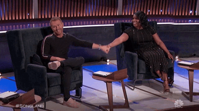 a man and woman are shaking hands while sitting in chairs on a stage .