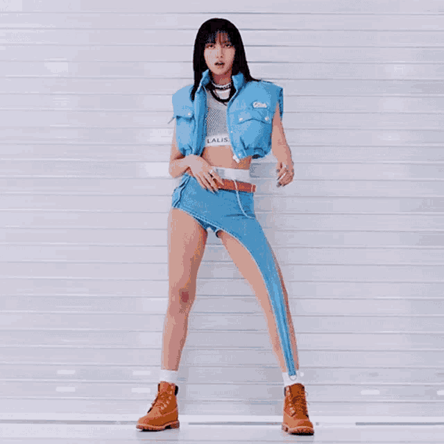 a woman wearing a blue vest and a denim skirt is standing in front of a white wall
