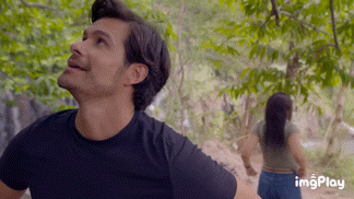 a man and a woman are standing in the woods holding hands .
