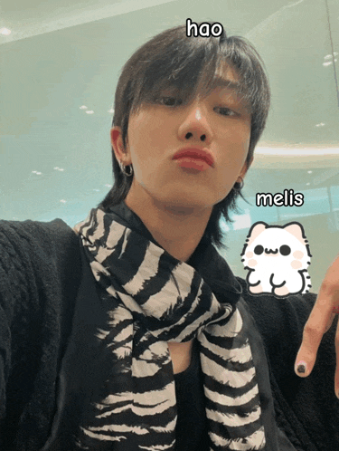 a man with a scarf around his neck has a sticker of a cat on his finger that says ' melis '
