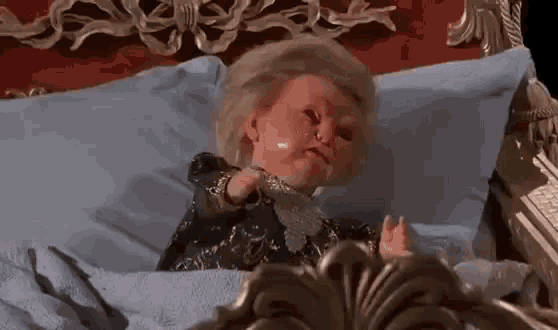 a doll is laying on a bed with a blue blanket and a mirror .