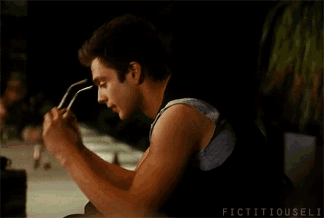 a man wearing sunglasses and a tank top is sitting at a table .