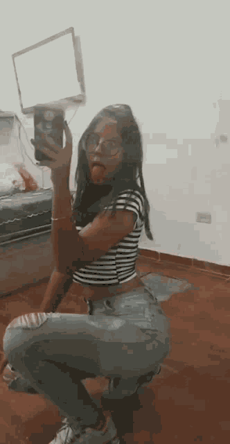 a young woman is taking a selfie in front of a mirror while wearing a striped shirt and jeans .