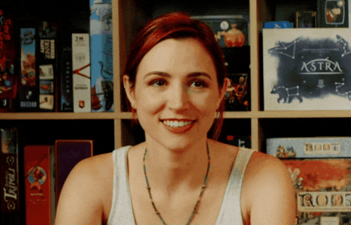 a woman smiles in front of a shelf full of board games including astra