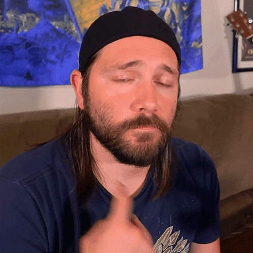 a man with a beard wearing a hat and a blue shirt