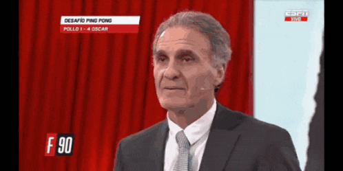 a man in a suit and tie stands in front of a red curtain and a sign that says f 90