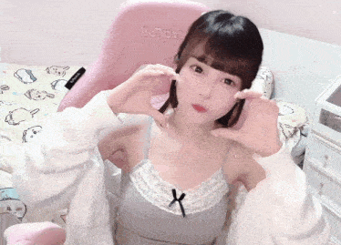a girl is making a heart shape with her hands in front of a pink chair that says ilu70