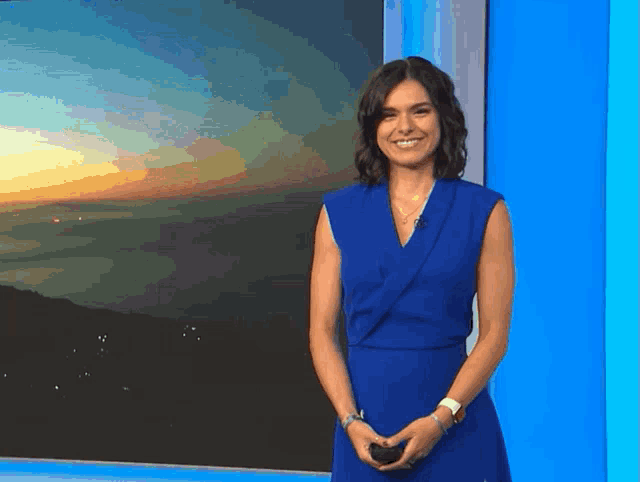 a woman in a blue dress is smiling in front of a blue wall