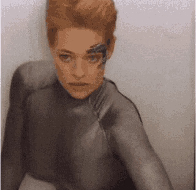 a woman in a gray suit with a tattoo on her face is standing in a room .