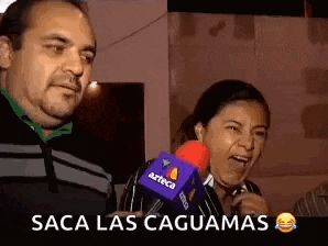a man and a woman are laughing while talking into a microphone with the words saca las caguas written above them .