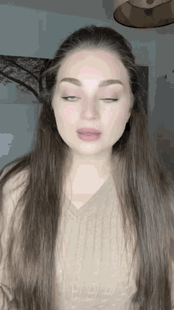 a woman with long hair is wearing a tan sweater and has her eyes closed
