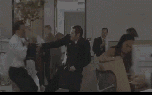 a group of people are fighting in a room while a woman holds a box .