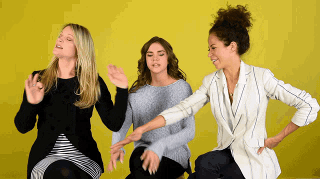 three women are dancing together in front of a yellow wall