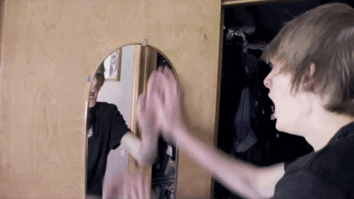 a young man is looking at his reflection in a mirror