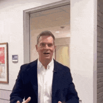 a man in a suit and white shirt is standing in front of a glass door and smiling .