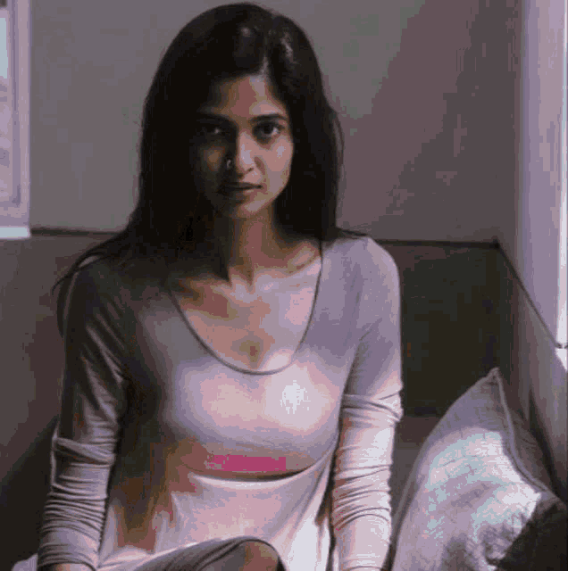 a woman in a pink shirt sits on a bed in front of a window
