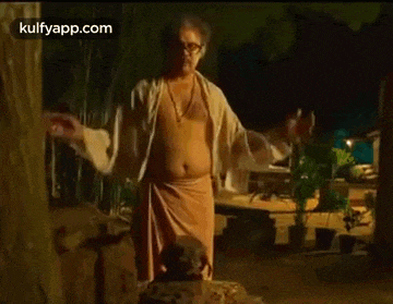 a man without a shirt is standing in front of a tree with his arms outstretched .