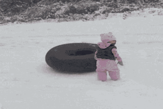 a little girl in pink standing next to a black tire