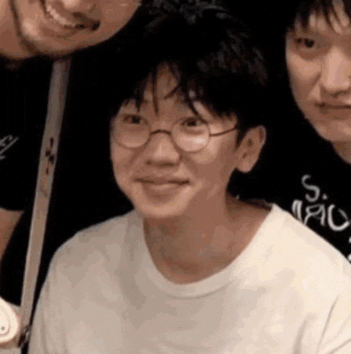 a young man wearing glasses and a white shirt is smiling while standing next to two other young men .
