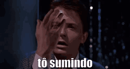 a man in a suit and tie is holding his hand to his face and saying `` to sumindo '' in a foreign language .