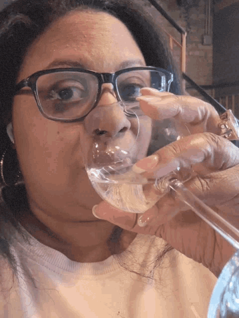 a woman wearing glasses is drinking from a clear glass