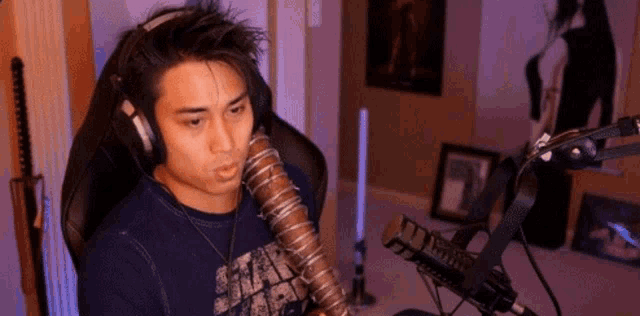 a man wearing headphones is sitting in front of a microphone and holding a walking dead stick .