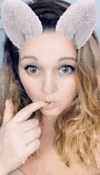 a woman wearing bunny ears covering her face with her finger
