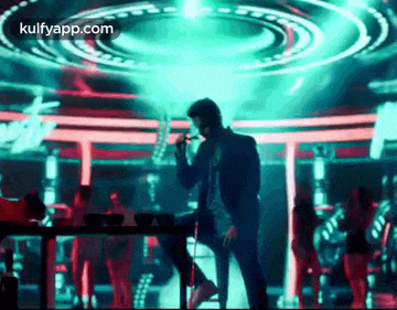 a man is singing into a microphone while sitting on a bar stool on a stage .