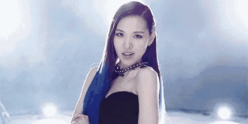 a woman with long blue hair and a black dress is standing in front of a blue background .