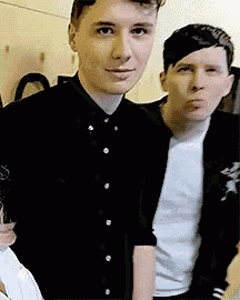two young men are standing next to each other in a room and one of them is wearing a black shirt .