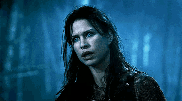 a woman with long dark hair and blue eyes is standing in the dark .