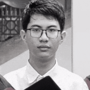 a young man wearing glasses and a white shirt holds a black book