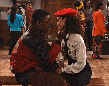 a man and woman are sitting on a bench and the man is wearing a red jacket with the letter r on the back