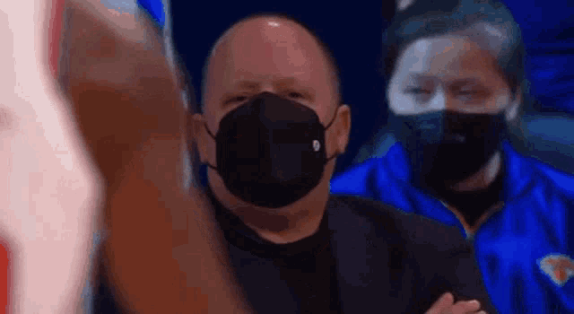 a man wearing a mask is sitting in a stadium watching a game .