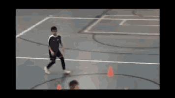 a boy in a blue shirt is kicking a soccer ball on a basketball court