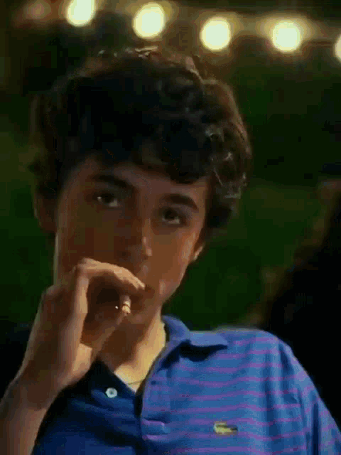 a young man with curly hair is wearing a blue and pink striped shirt and holding a sandwich .