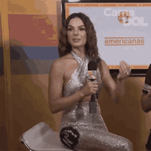 a woman in a silver dress is holding a microphone