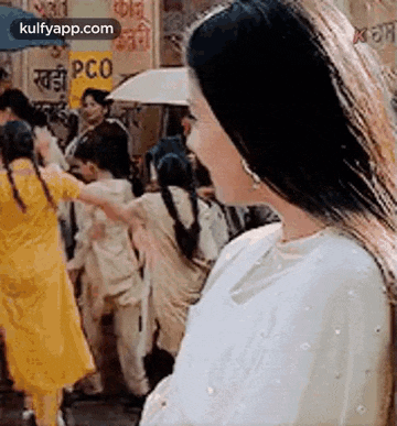 a woman in a white dress is standing in a crowd of people on a street .
