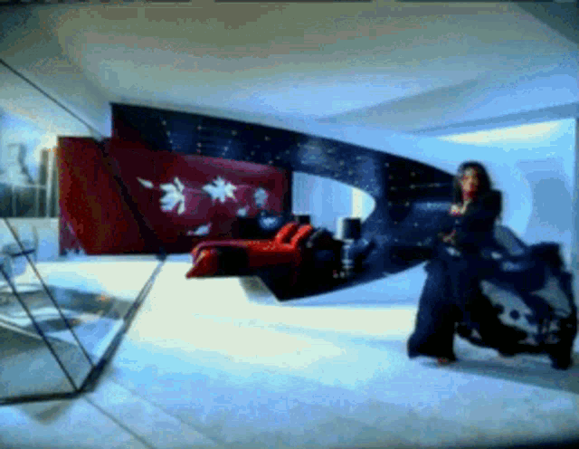 a woman in a black dress stands in a room with a red couch