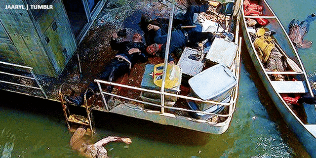 a man is laying on a boat in the water next to a canoe .