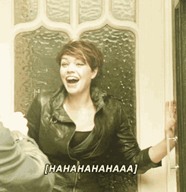 a woman in a leather jacket is laughing in front of a door that says ' hahahahaaa '