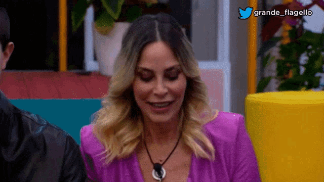 a woman wearing a purple top and a necklace with the hashtag grande flagello on the bottom