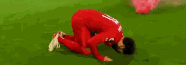 a soccer player is kneeling down on the field with pink smoke coming out of his knee .