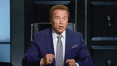 arnold schwarzenegger is wearing a blue suit and tie and has a ring on his finger .